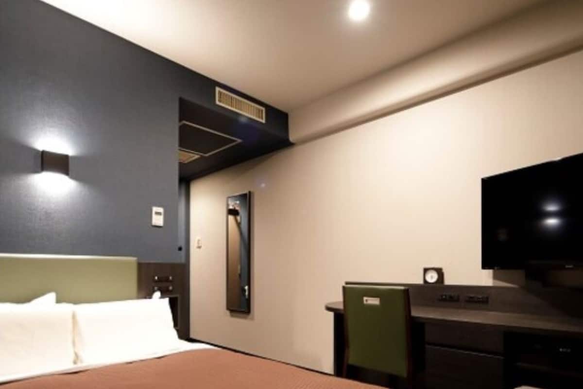 A hotel room with a large bed, a desk with a computer, a television, and a mirror.