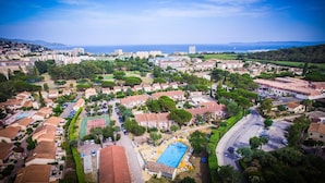 An aerial view of a coastal town with residential buildings, a large swimming pool, and a road curving through the area. - Vacances Passion La Grande Bastide (Le Lavandou)