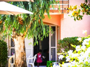Un enfant sort d’un bâtiment. On aperçoit un arbre et une chaise blanche au premier plan.