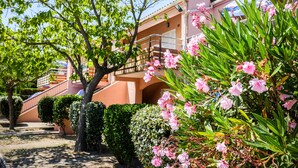 A building with a red facade, a balcony, and pink flowers in the foreground. - Vacances Passion La Grande Bastide (Le Lavandou)