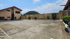 A parking lot with marked spaces, a building with a red roof, and a security fence. - Hotel Resort Obelisco (La Asunción)
