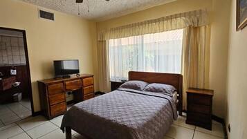Una habitación de hotel con cama, televisión, cómoda, espejo y ventana con cortinas.