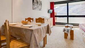 A hotel room with a dining table set for two, a bed with a view, a TV, and a large window.