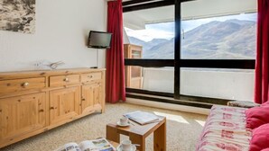 A room with a wooden cabinet, a television, a small table with a cup and a book, and a bed with a pink blanket.