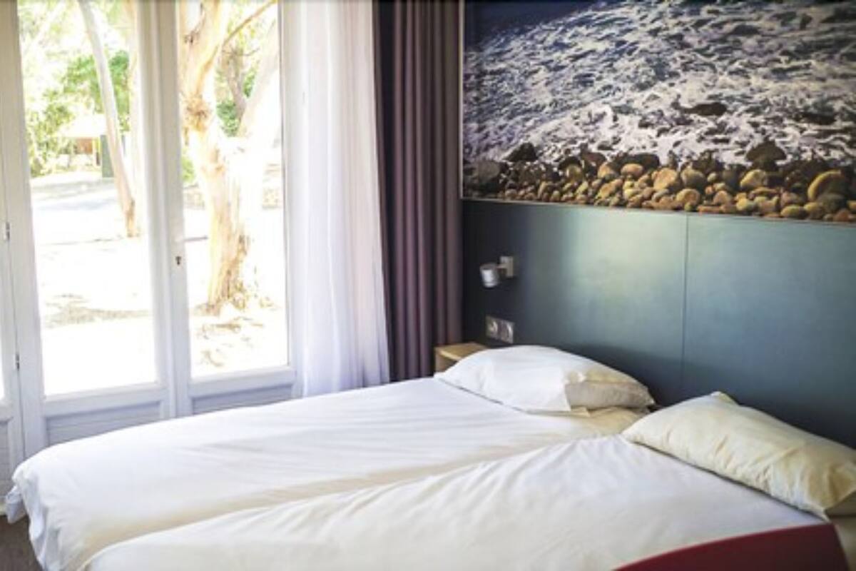 A bed with white linens, a window with curtains, and a wall with a textured design.