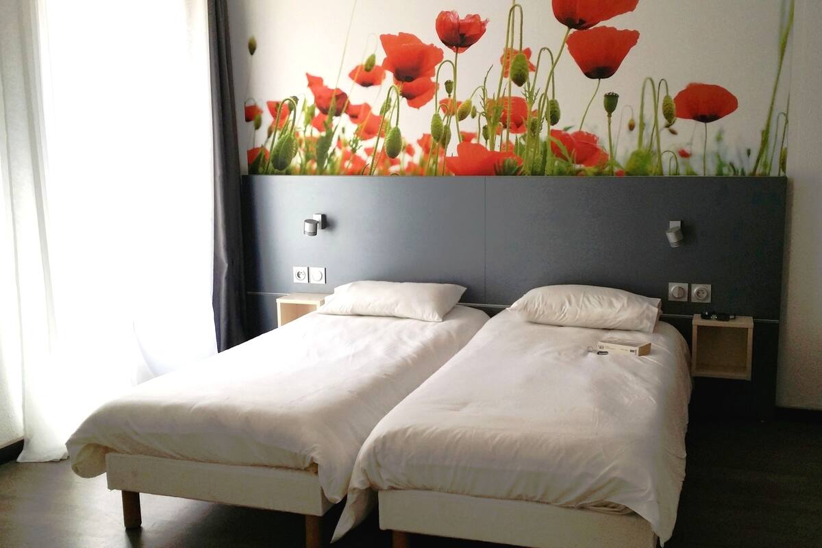 A hotel room with two single beds, a large wall-mounted TV, and a decorative wall with red flowers.