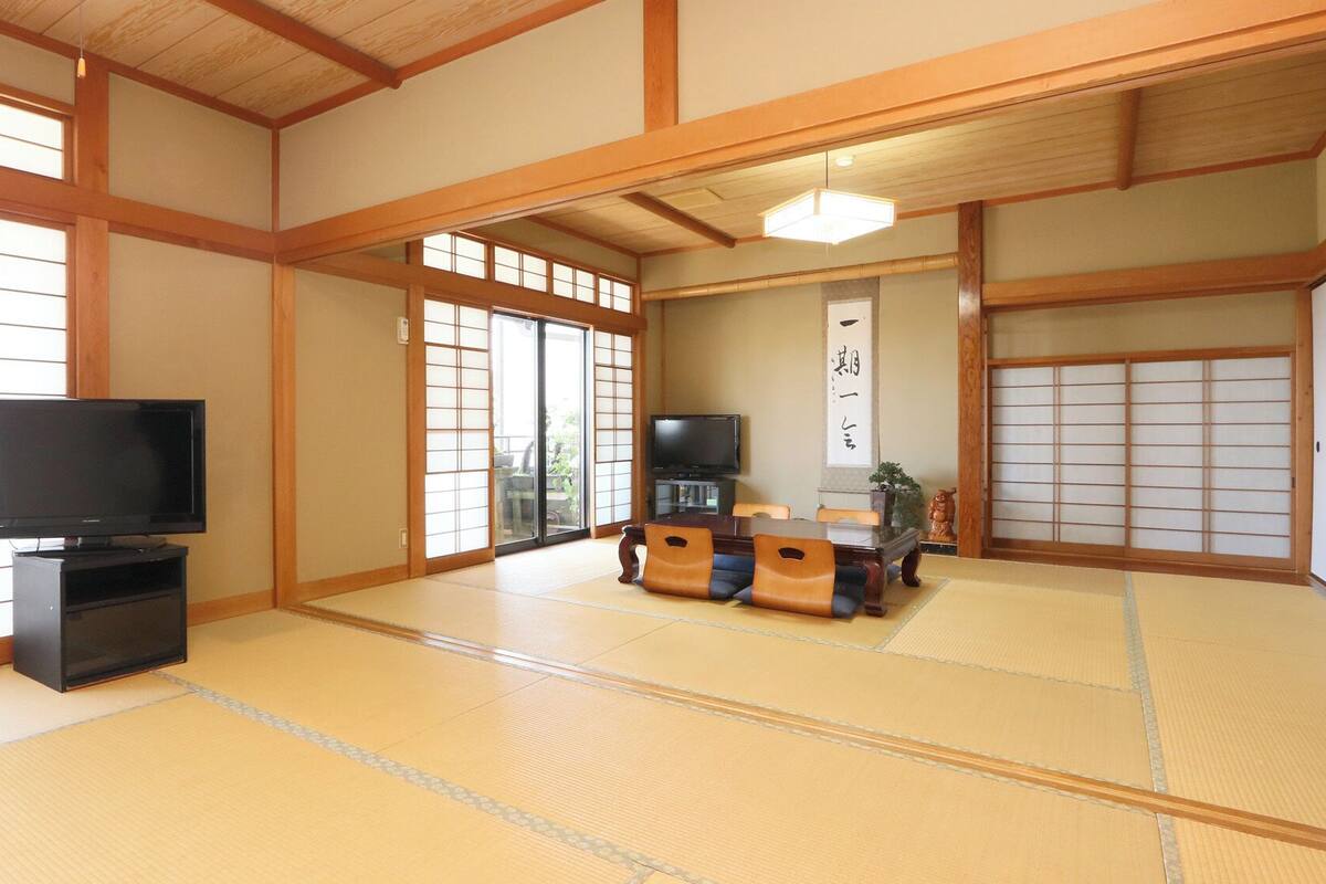 A traditional Japanese room with tatami flooring, a television, a sliding door, and a tatami mat table.
