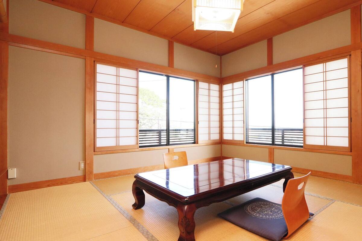 A traditional Japanese room with tatami flooring, a low table, sliding shoji doors, and a television.