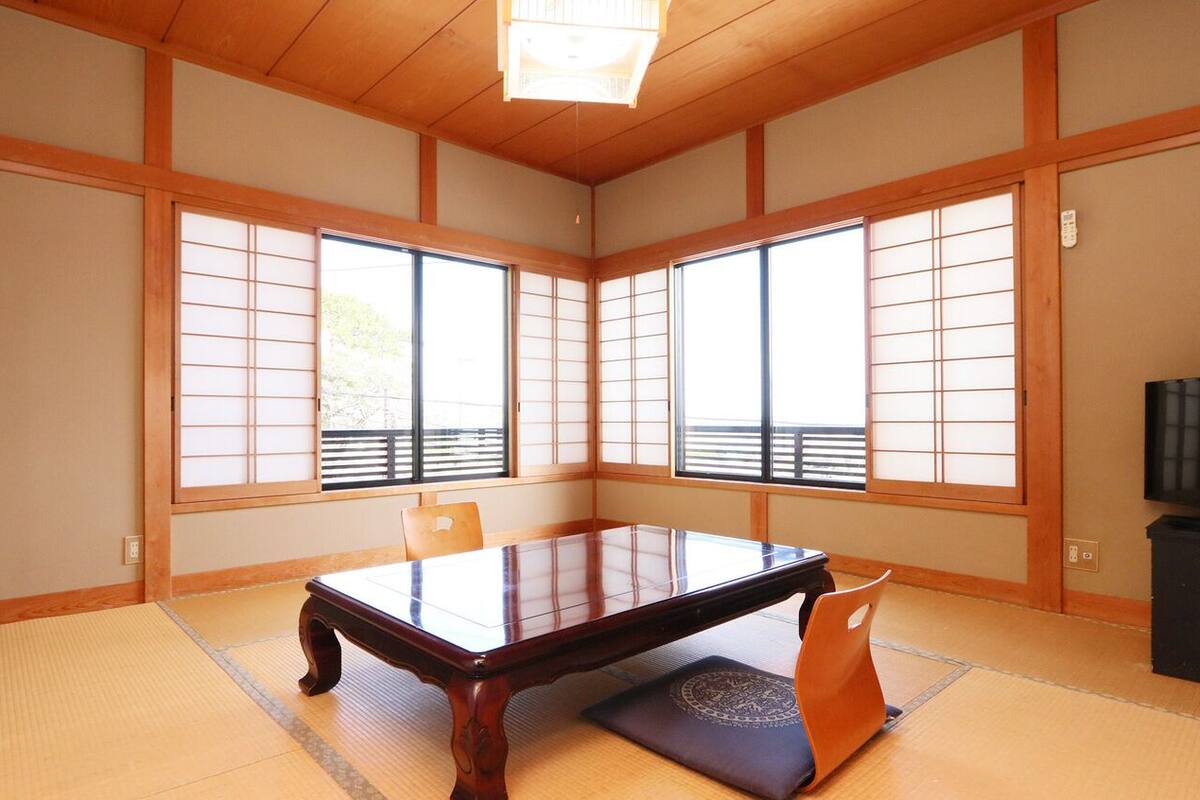 A traditional Japanese room with tatami flooring, a low table, sliding doors, and a television.