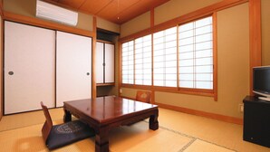 Ein traditioneller japanischer Raum mit Tatami-Boden, einem niedrigen Holztisch, einem Fernseher auf einem Standfuß, Schiebetüren und einem großen Fenster mit Shoji-Bildschirmen.