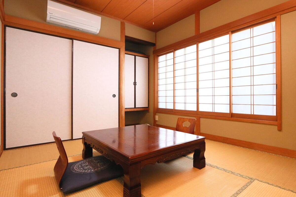 A traditional Japanese room with tatami flooring, a low table, a chair, sliding doors, and a TV on a stand.