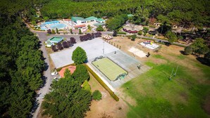 Vista aérea de un complejo turístico con varias edificaciones, una amplia piscina, canchas de tenis y zonas boscosas circundantes.