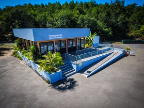 A modern building with a blue exterior, large windows, and a covered outdoor area with steps leading to a balcony. - Vacances Passion - Leon Les Genets (Léon)