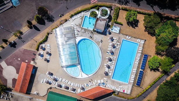 Vista aérea de un complejo turístico con varias piscinas, tumbonas y un estacionamiento.