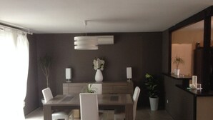 Un comedor moderno con una mesa rectangular, cuatro sillas blancas, un florero con flores y una lámpara colgante.