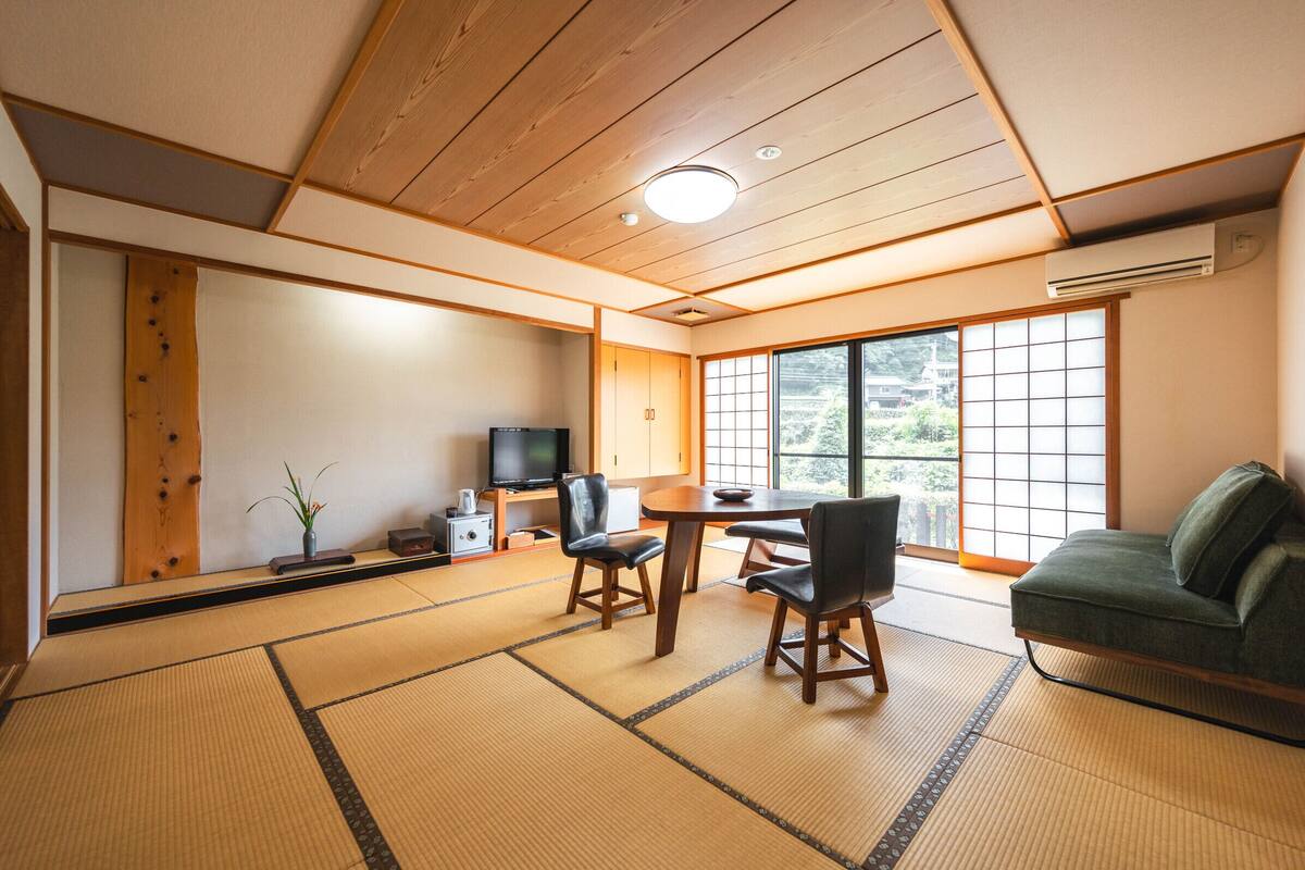 Une pièce de style japonais traditionnel, avec un sol recouvert de tatamis, une table basse, des chaises, un téléviseur et un canapé.