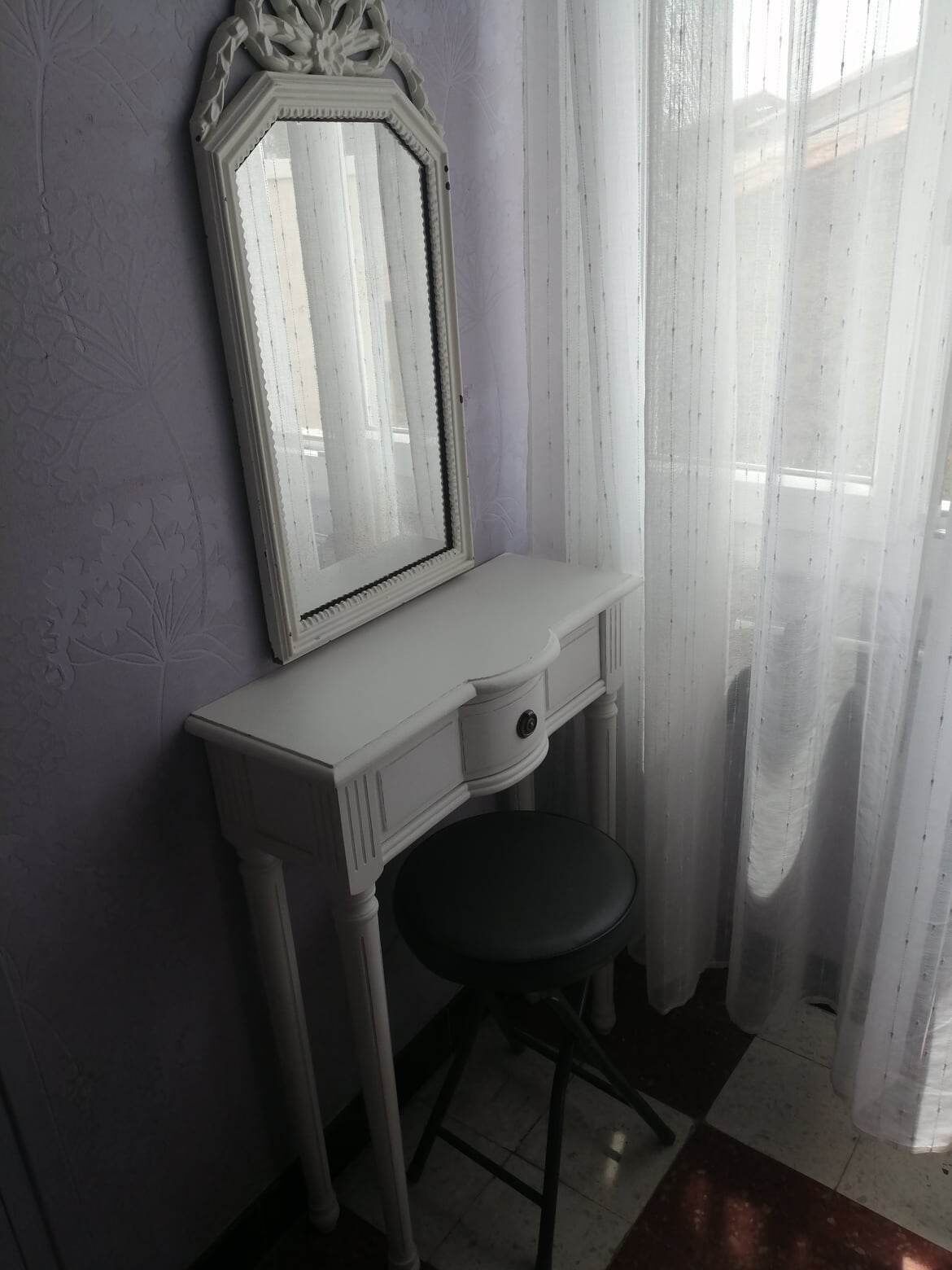 A white vanity with a mirror, a small stool, and a drawer.