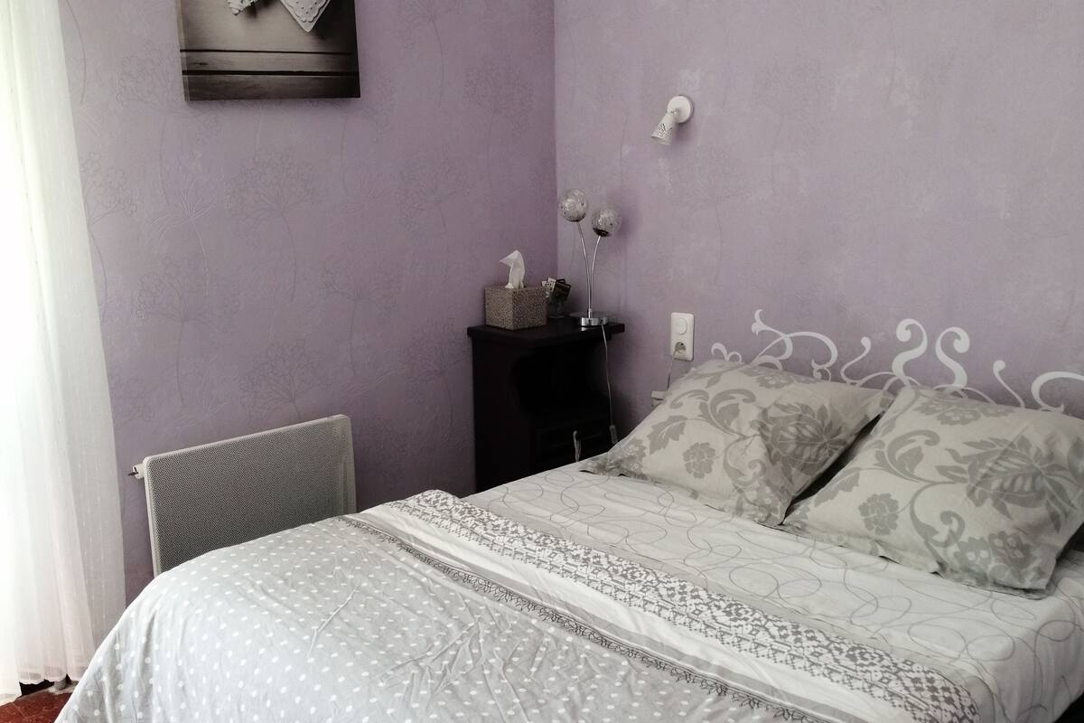 A bedroom with a bed, a nightstand, a radiator, and a wall-mounted heater.