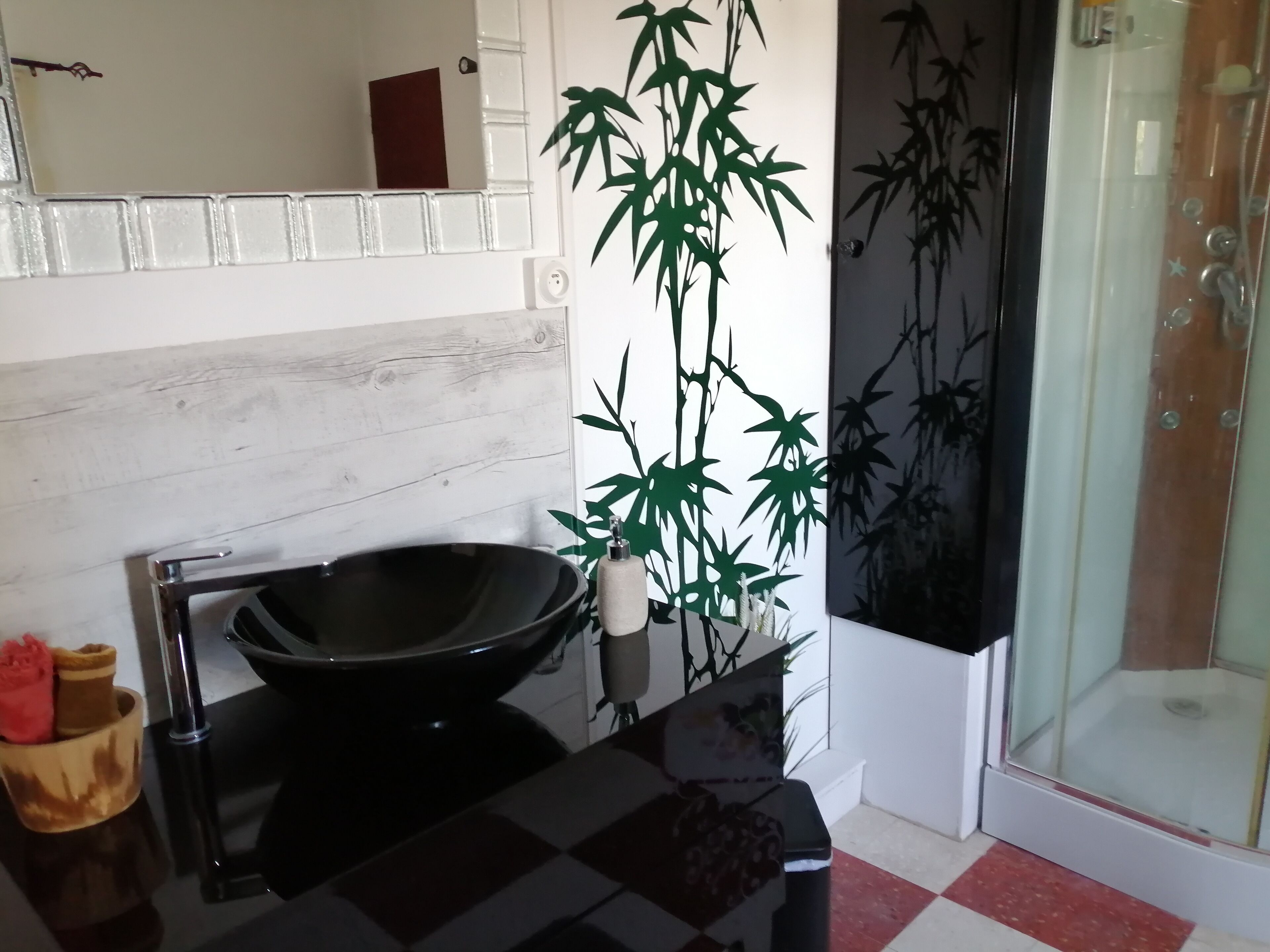 Une salle de bain avec un lavabo noir, un miroir, une plante en bambou et une cabine de douche en verre.
