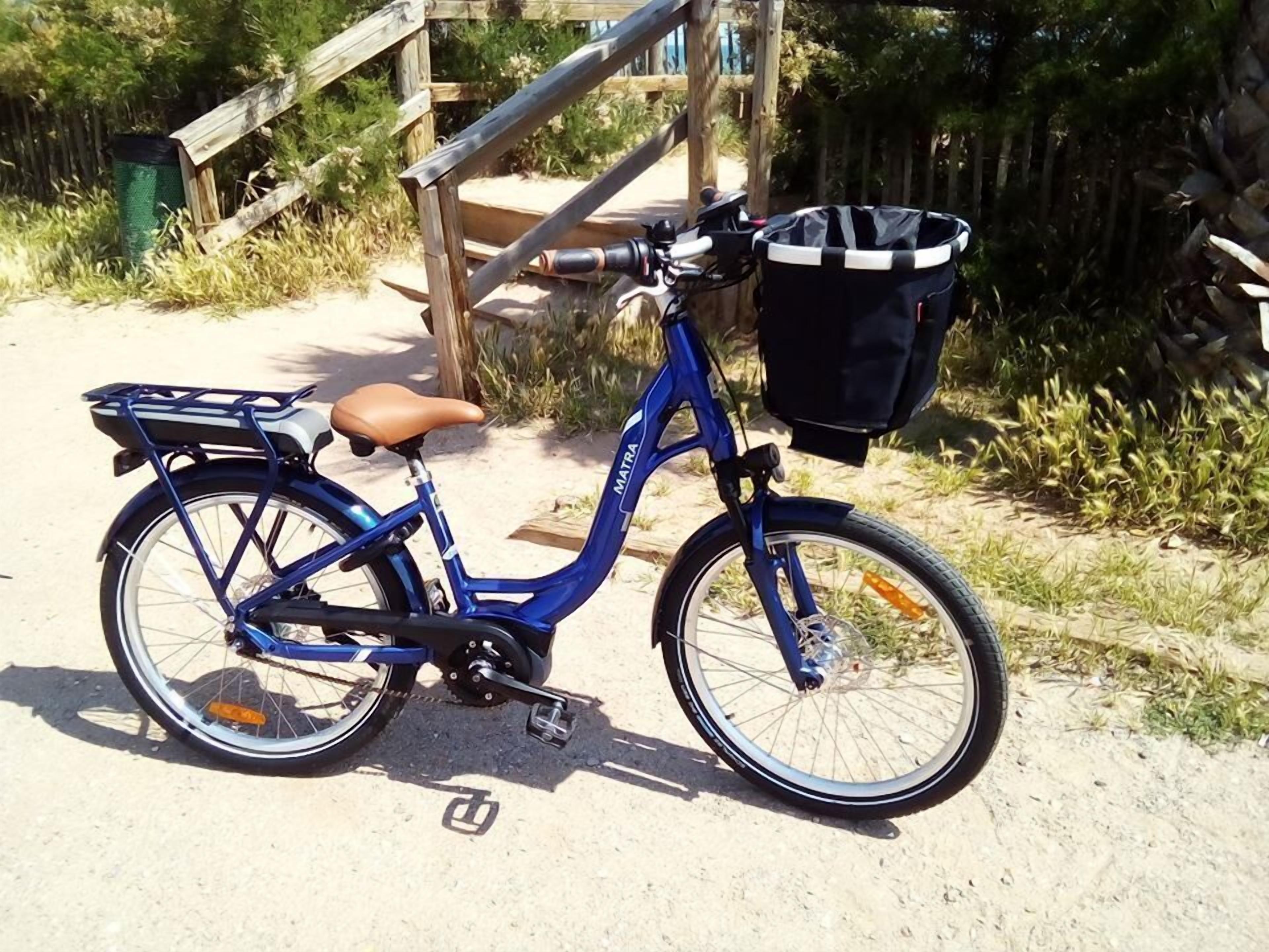 A blue bicycle with a basket and a brown seat parked on a sandy path.