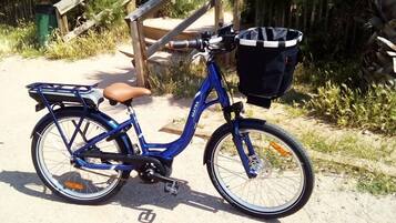 A blue bicycle with a basket and a brown seat parked on a sandy path.