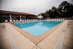 A swimming pool with lounge chairs and a building with a tiled roof in the background. - Vacances Passion Les Bris (Saint-Trojan-les-Bains)