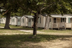A row of mobile homes with a grassy area and trees in the foreground. - Vacances Passion Les Bris (Saint-Trojan-les-Bains)