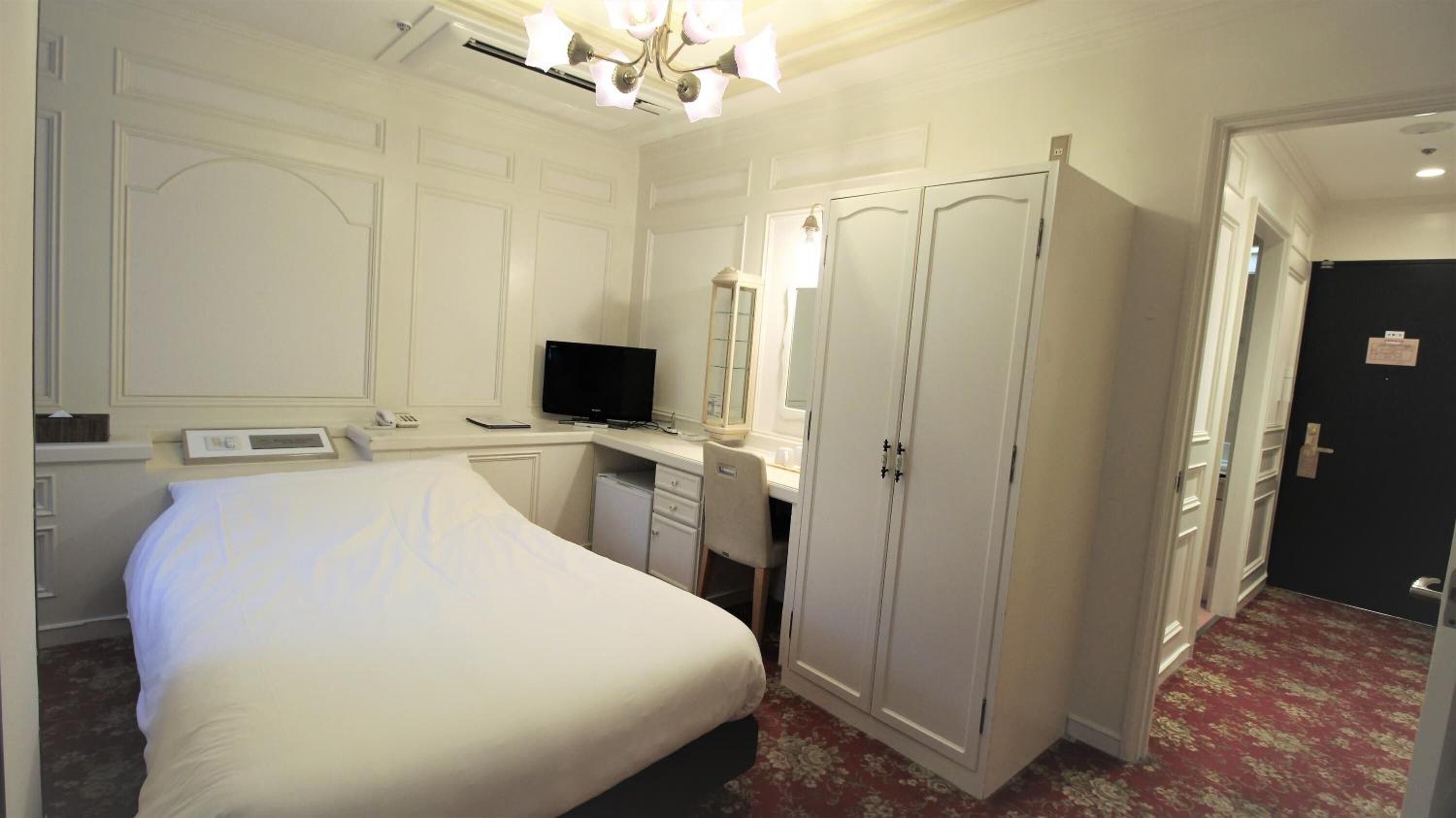 A hotel room with a bed, a desk with a computer, a television, and a wardrobe.