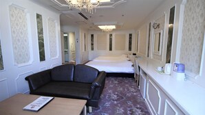 A hotel room with a double bed, a sofa, a small table with a menu, and a minibar. - Royal Hotel Shinokubo (Tokyo)
