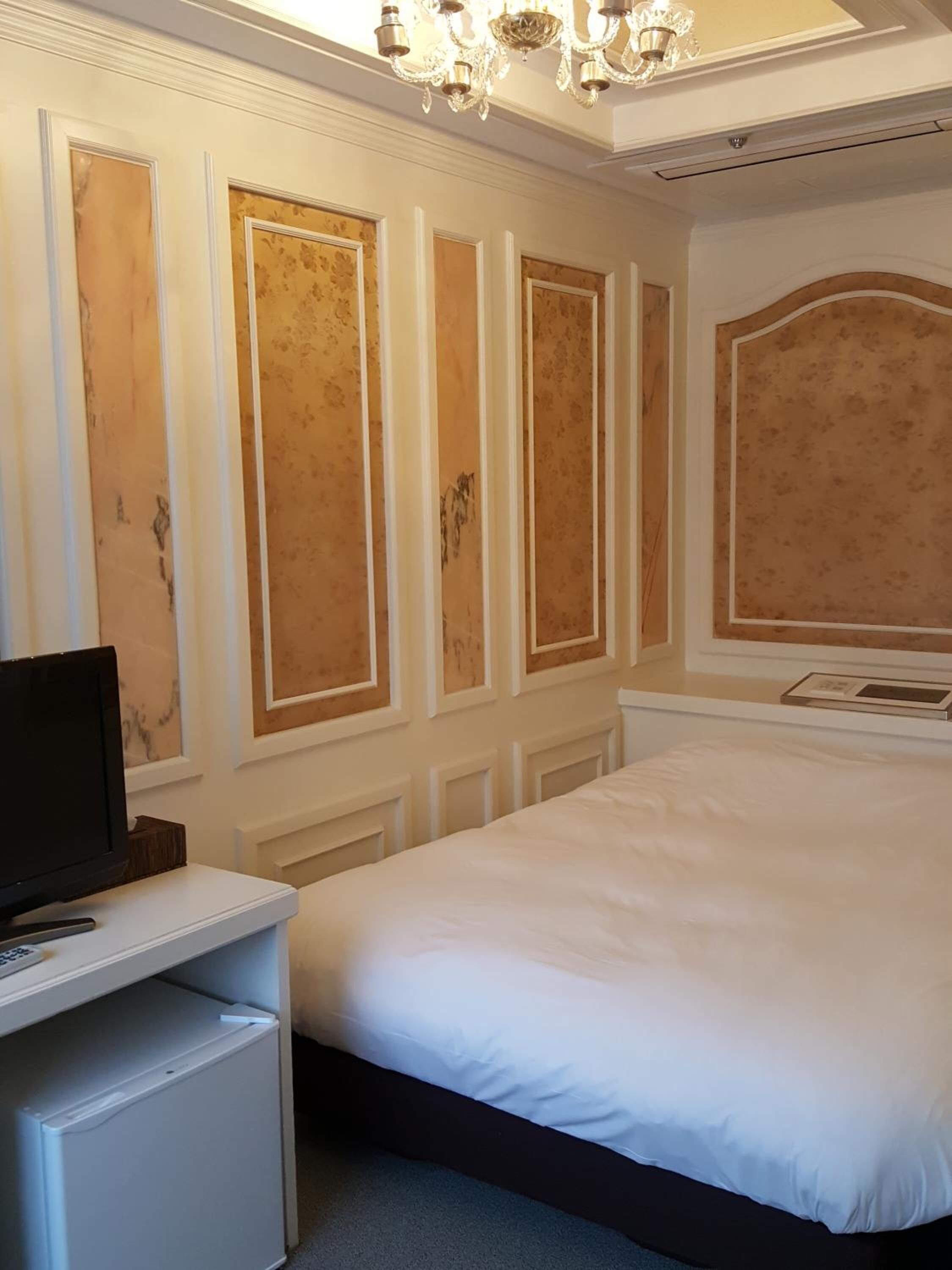 A hotel room with a bed, a desk with a television, and a chandelier.
