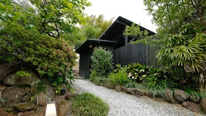 A garden pathway leading to a wooden structure with a sloped roof, surrounded by various plants and rocks. - Albergo Yuraku (Yugawara)