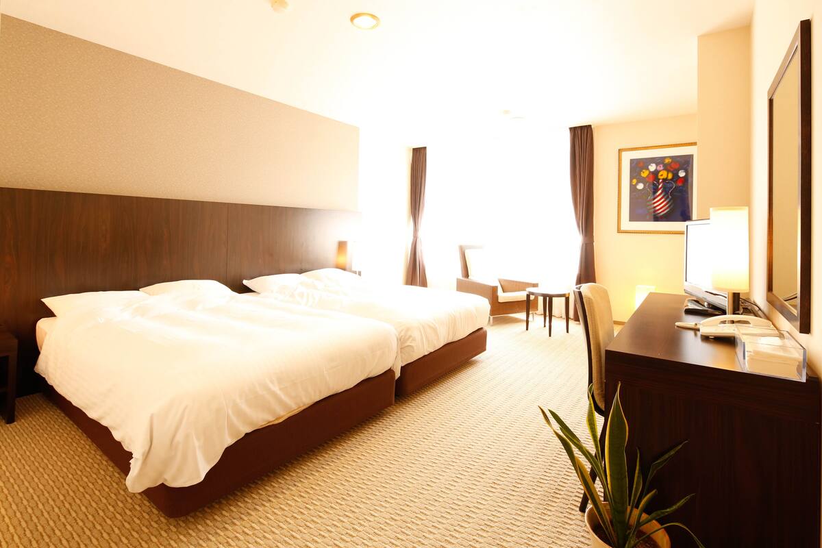 Ein Hotelzimmer mit einem großen Bett, einem Schreibtisch, einem Stuhl und einer Zimmerpflanze.