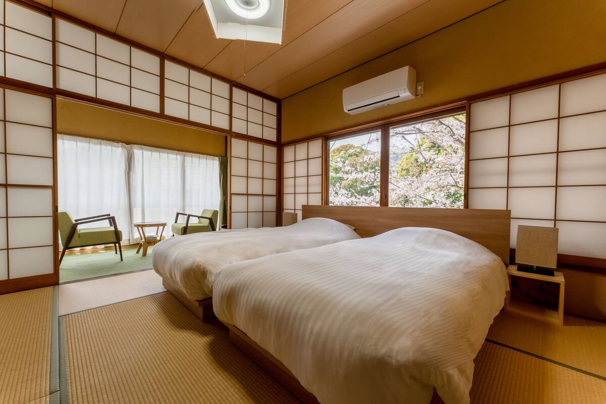 Ein traditioneller japanischer Raum mit Tatami-Böden, zwei Betten, einer Schiebetür und Blick auf Kirschblüten.