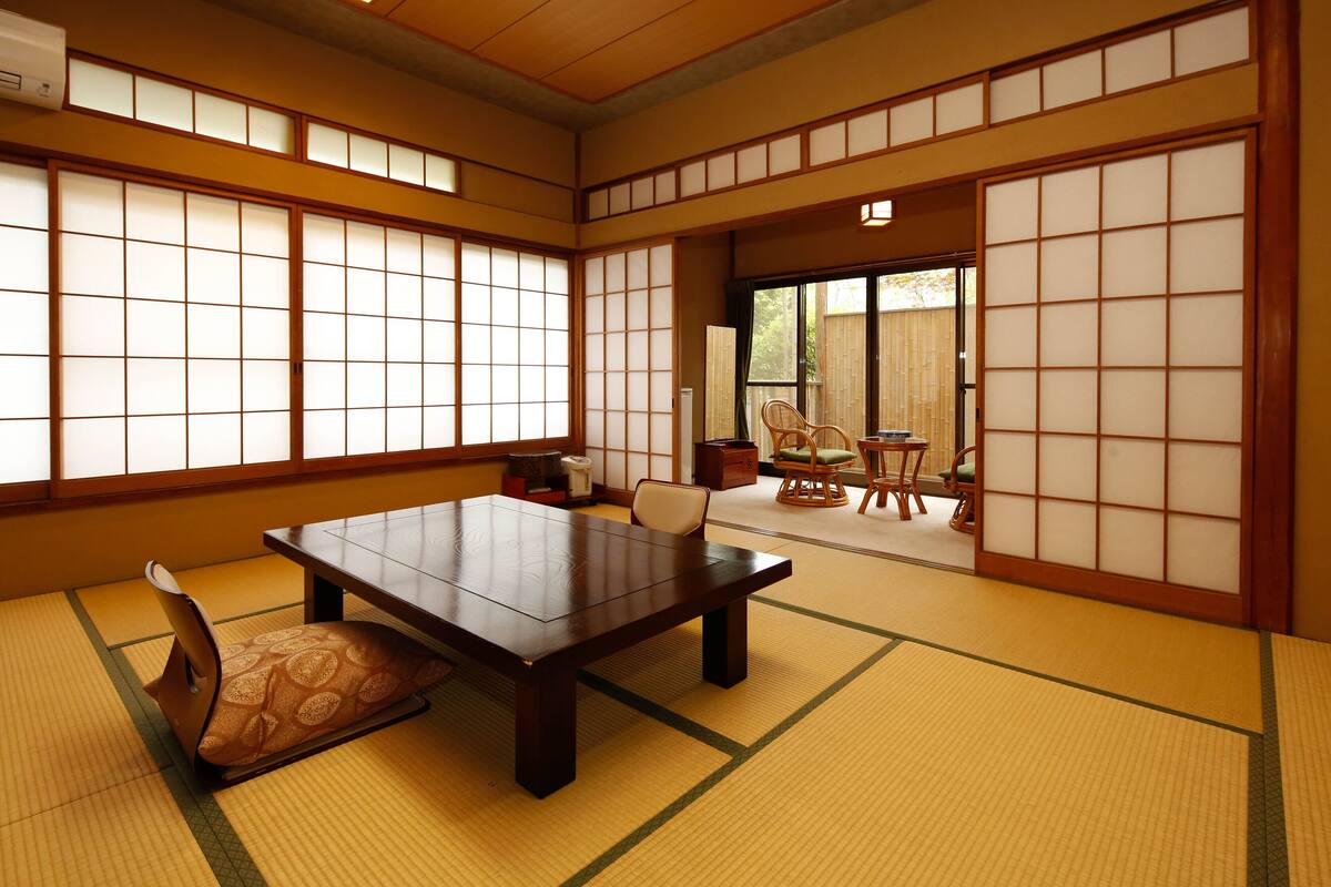 Ein traditioneller japanischer Raum mit Tatami-Boden, einem niedrigen Tisch mit Kissen und Schiebetüren.