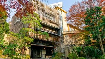 A traditional Japanese building with a wooden facade, a black entrance, and a garden with various plants and trees.