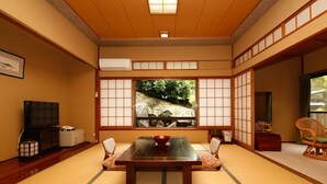 A traditional Japanese room with tatami flooring, a low table with a red bowl, sliding doors, and a view of a garden. - Albergo Yuraku (Yugawara)