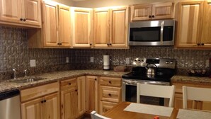 A kitchen with wooden cabinets, a stainless steel microwave, a stove, and a dining table with chairs.