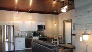 A modern kitchen with white cabinets, a stainless steel refrigerator, a microwave, and a dining area with a black leather couch and a table.