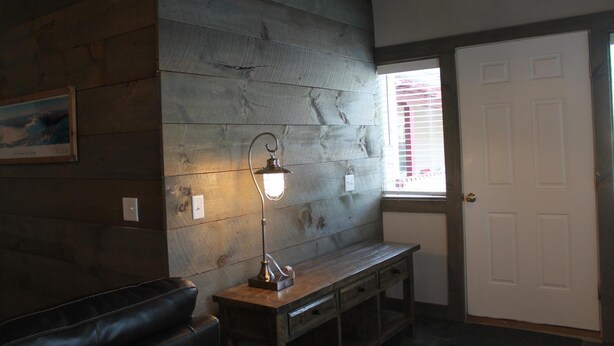 A room with a wooden wall, a bench, a desk, a lamp, and a door.