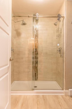 A glass-enclosed shower with a rain showerhead, a handheld showerhead, and a glass door. - Strictly Moose Luxury Vacation Suites (Gorham)