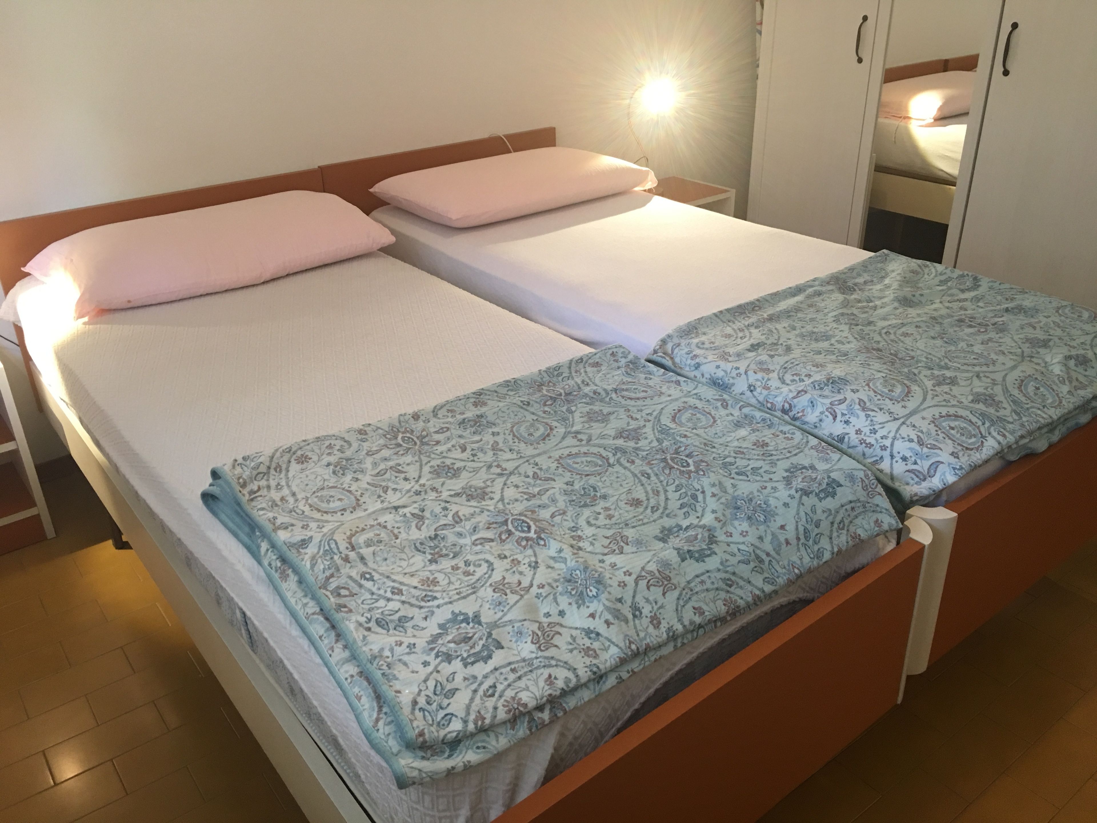 A double bed with a patterned bedspread, two pillows, and a bedside table with a lamp.