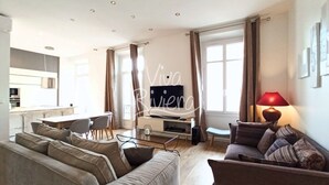Un soggiorno moderno con un divano, un tavolino e una televisione. In secondo piano, si intravede una zona cucina.