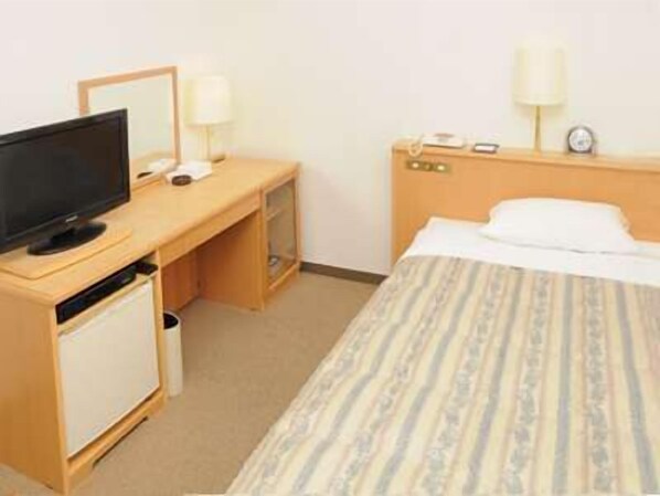Una habitación de hotel con una cama, un escritorio con computadora, un televisor y una lámpara.