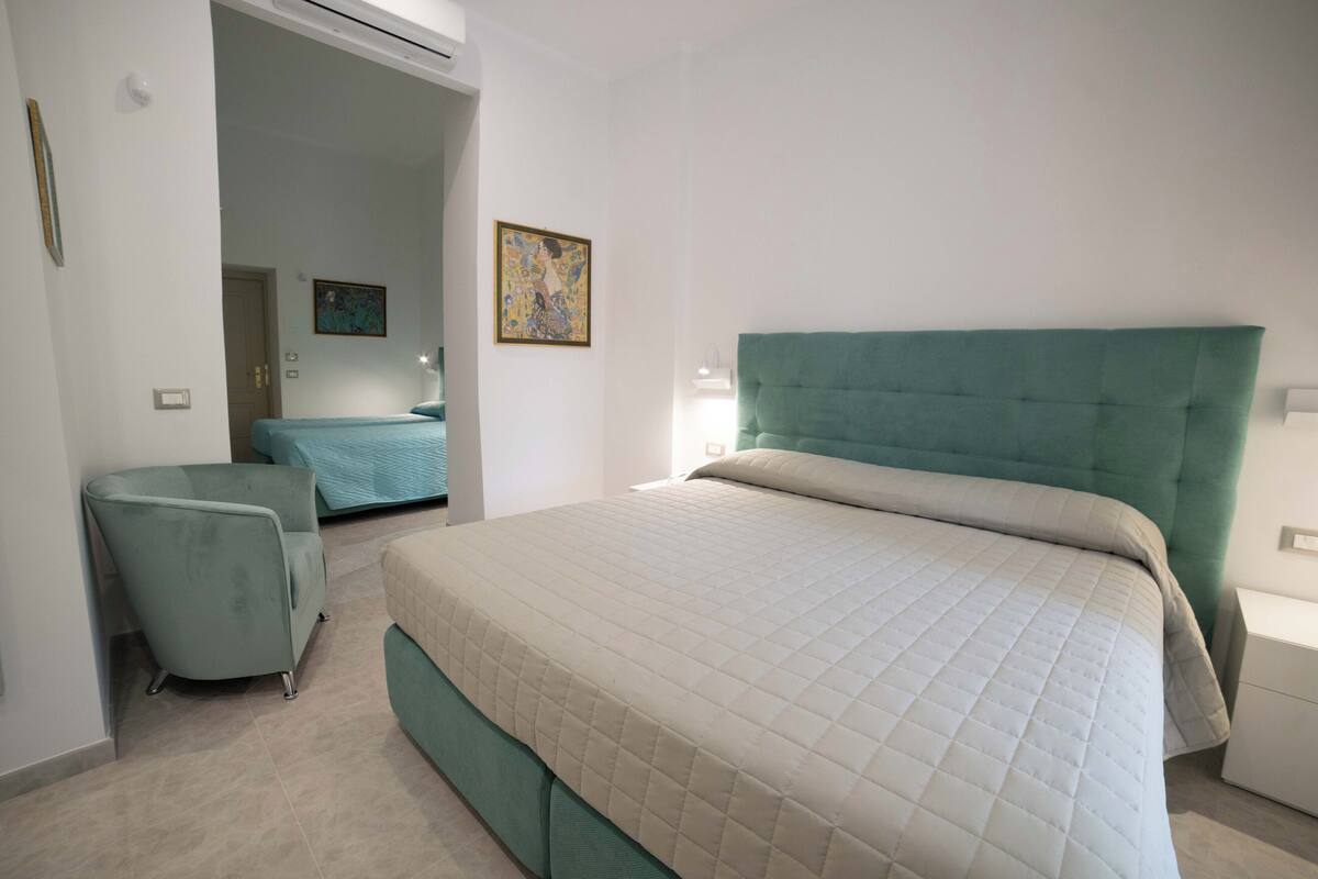 Un dormitorio con una cama grande, una silla, una mesita de noche y un cuadro en la pared.