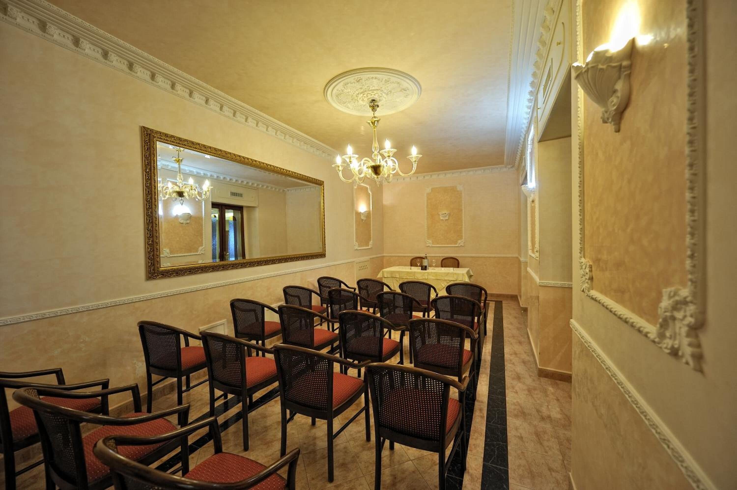 Ein Konferenzraum mit einem großen Spiegel, einer Chandelüster und Reihen von Stühlen.