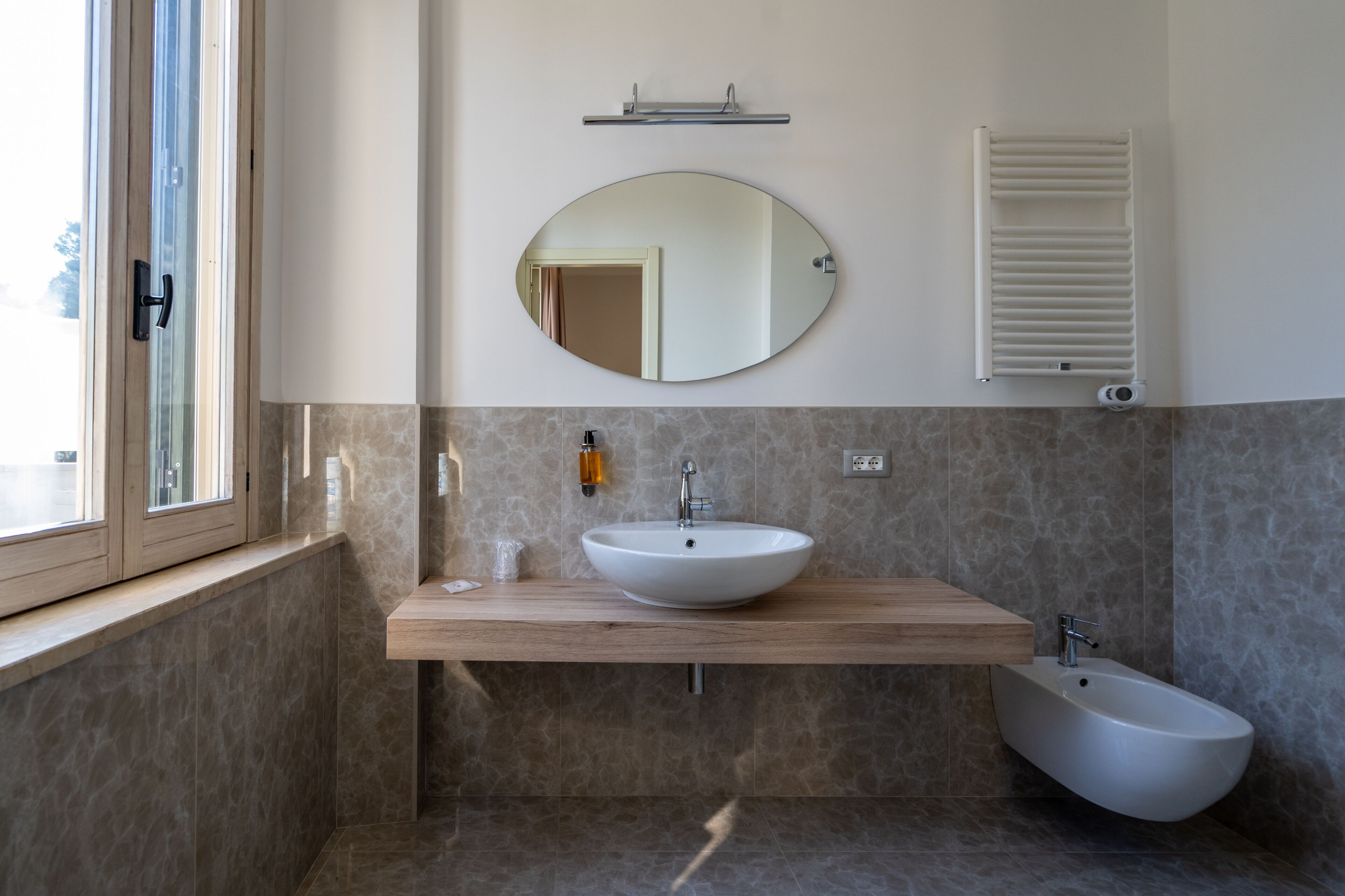 Et moderne badeværelse med et træbord, et rundt spejl, en bidet og en håndklædestang.