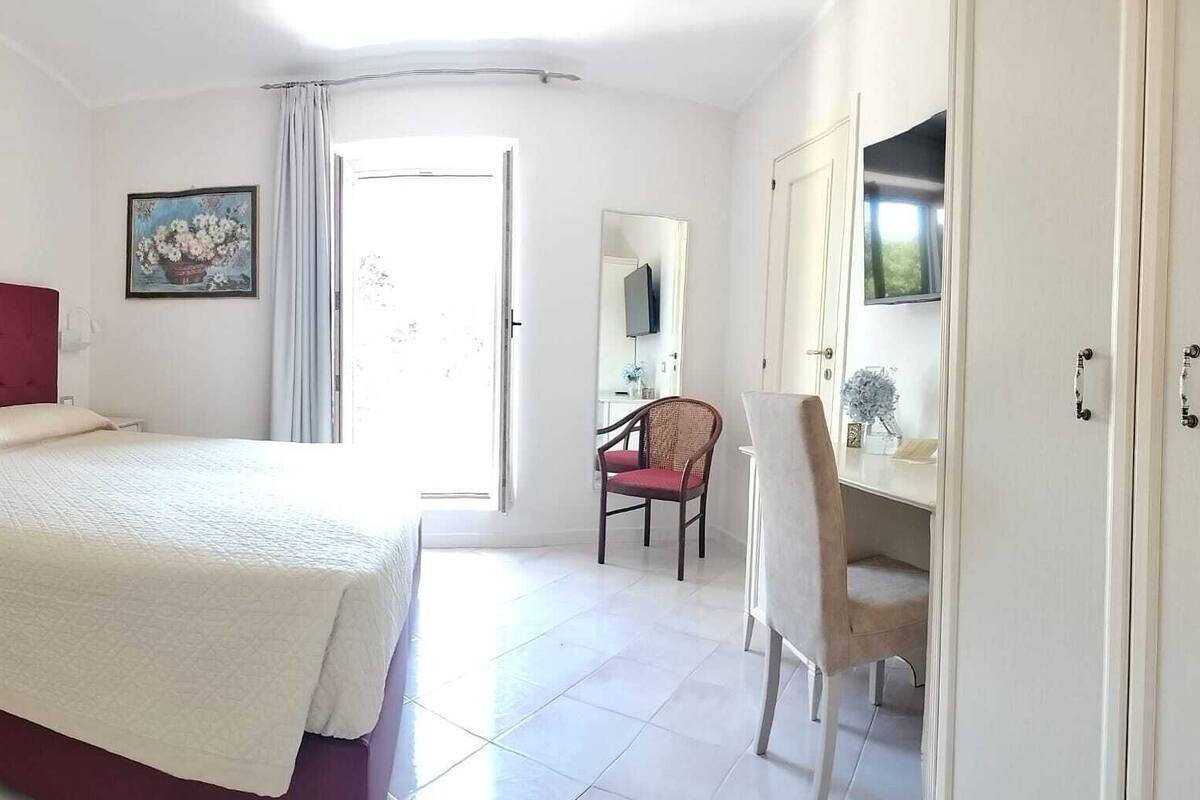 Un dormitorio con una cama, una mesita de noche, una silla, un escritorio, un espejo y un armario.