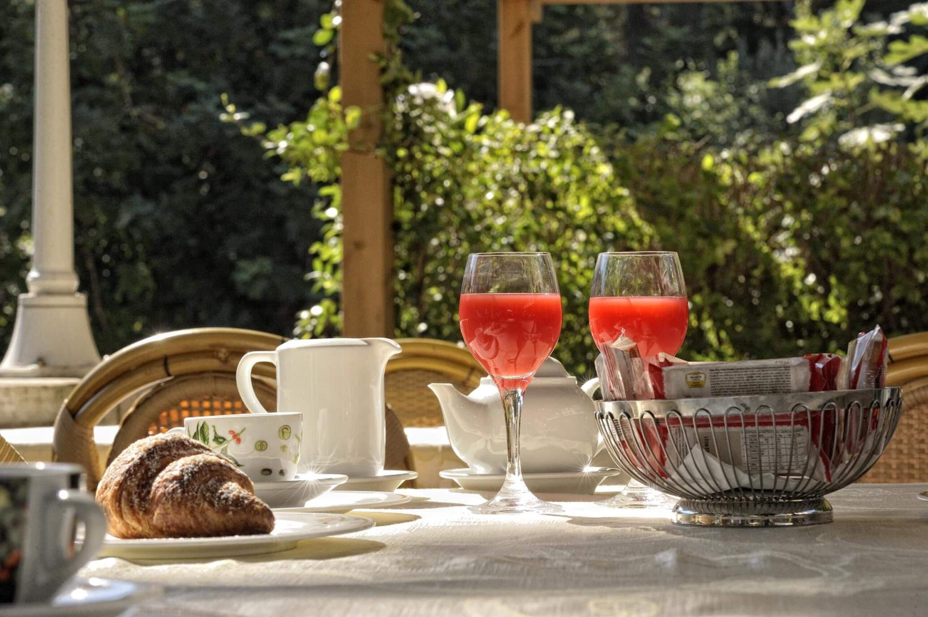 Frühstücksaufteilung mit Croissants, einer Zeitungskorb und zwei Gläsern roter Saft an einem Tisch im Freien.