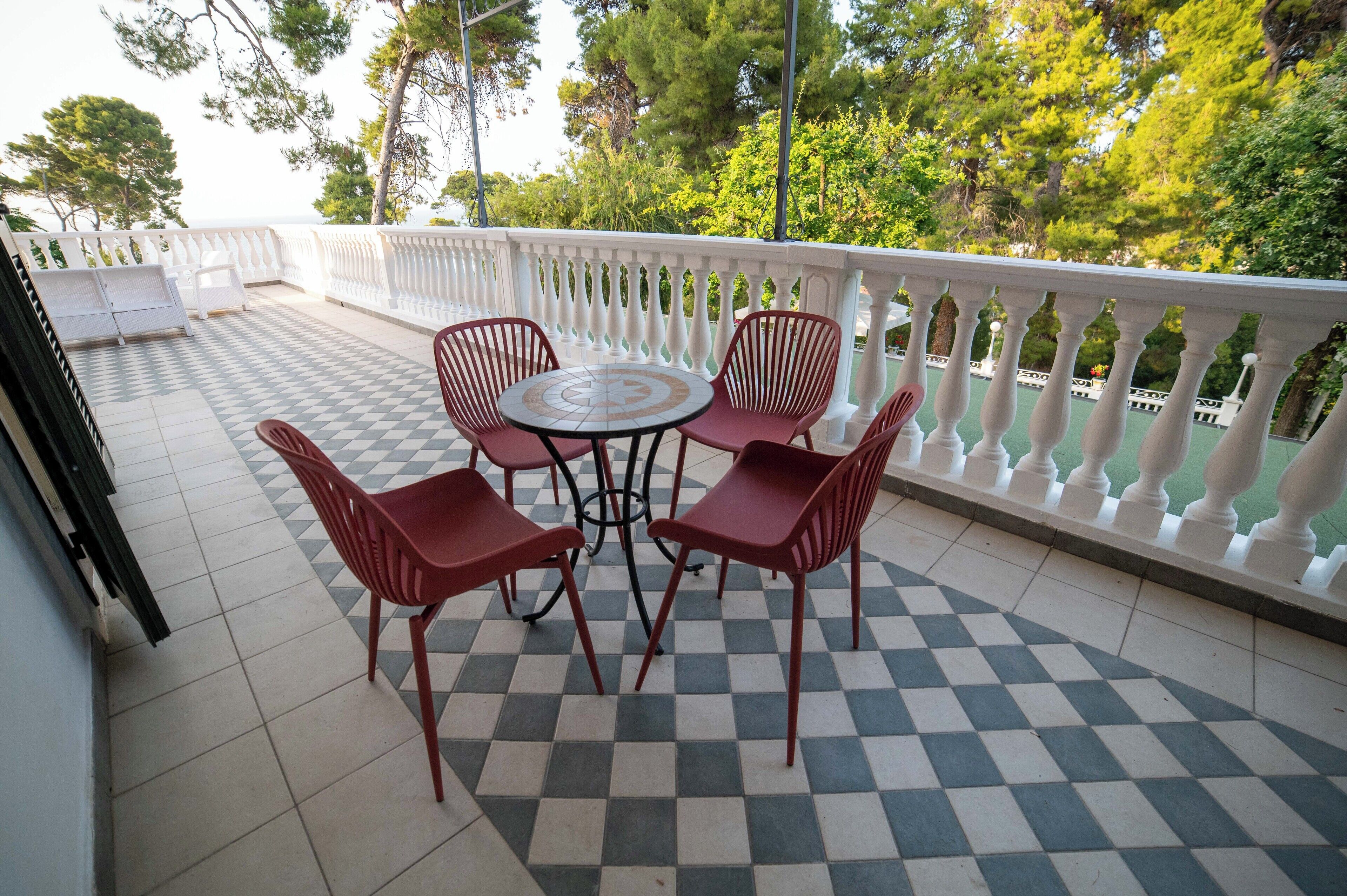 A terrace with a checkered floor, a round table, and four red chairs.