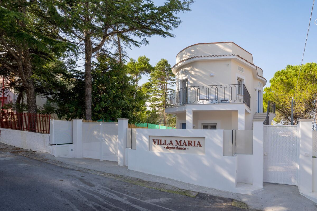 Een moderne villa met een balkon, omgeven door een witte hek en bomen.